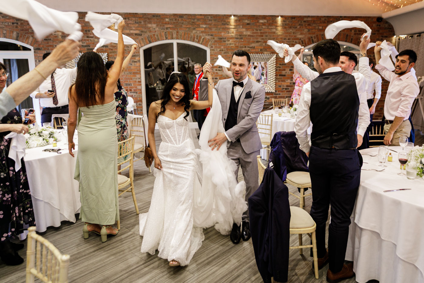bride and groom enter reception with guests waving napkins