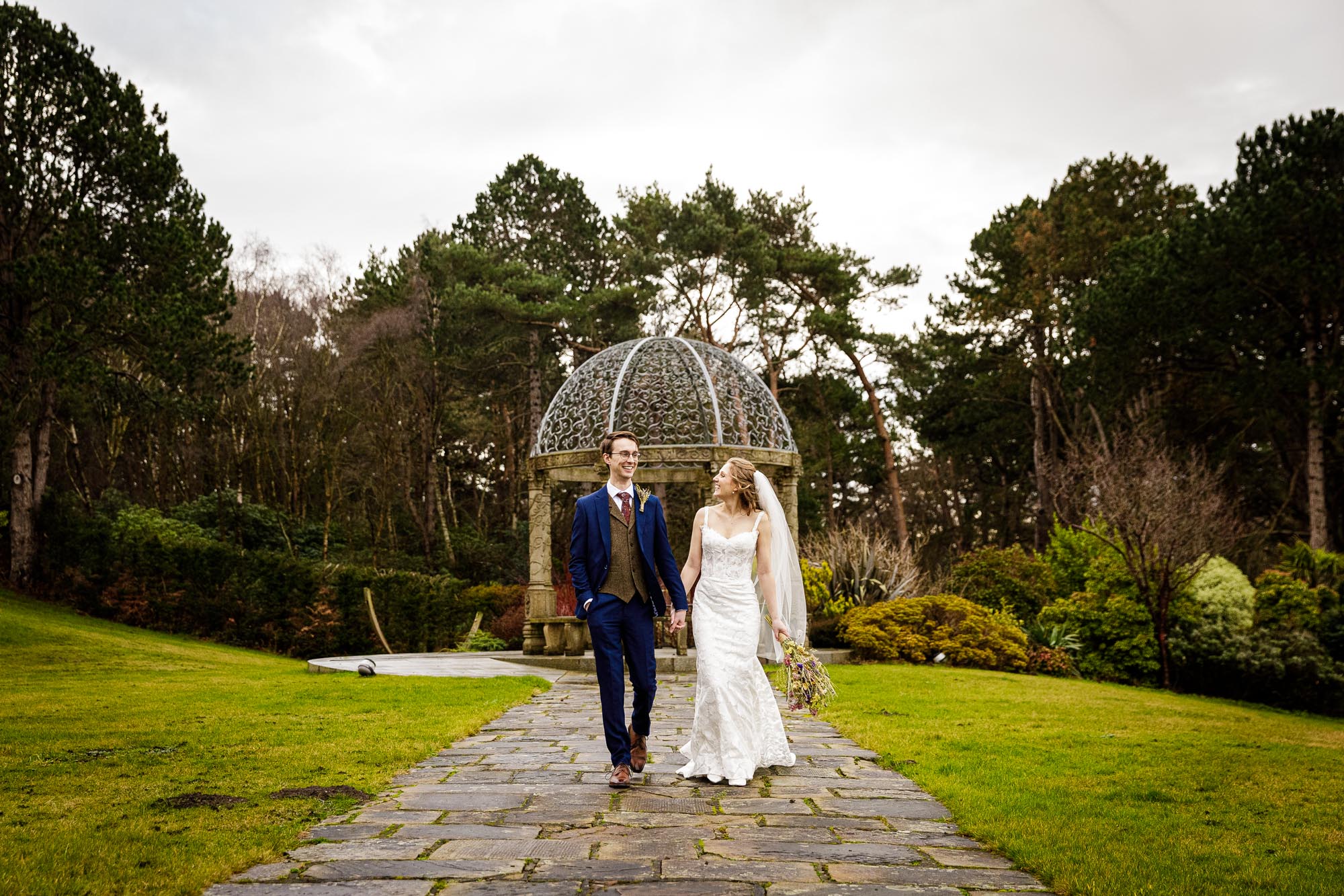 bride and groom walking holding hands in gardens