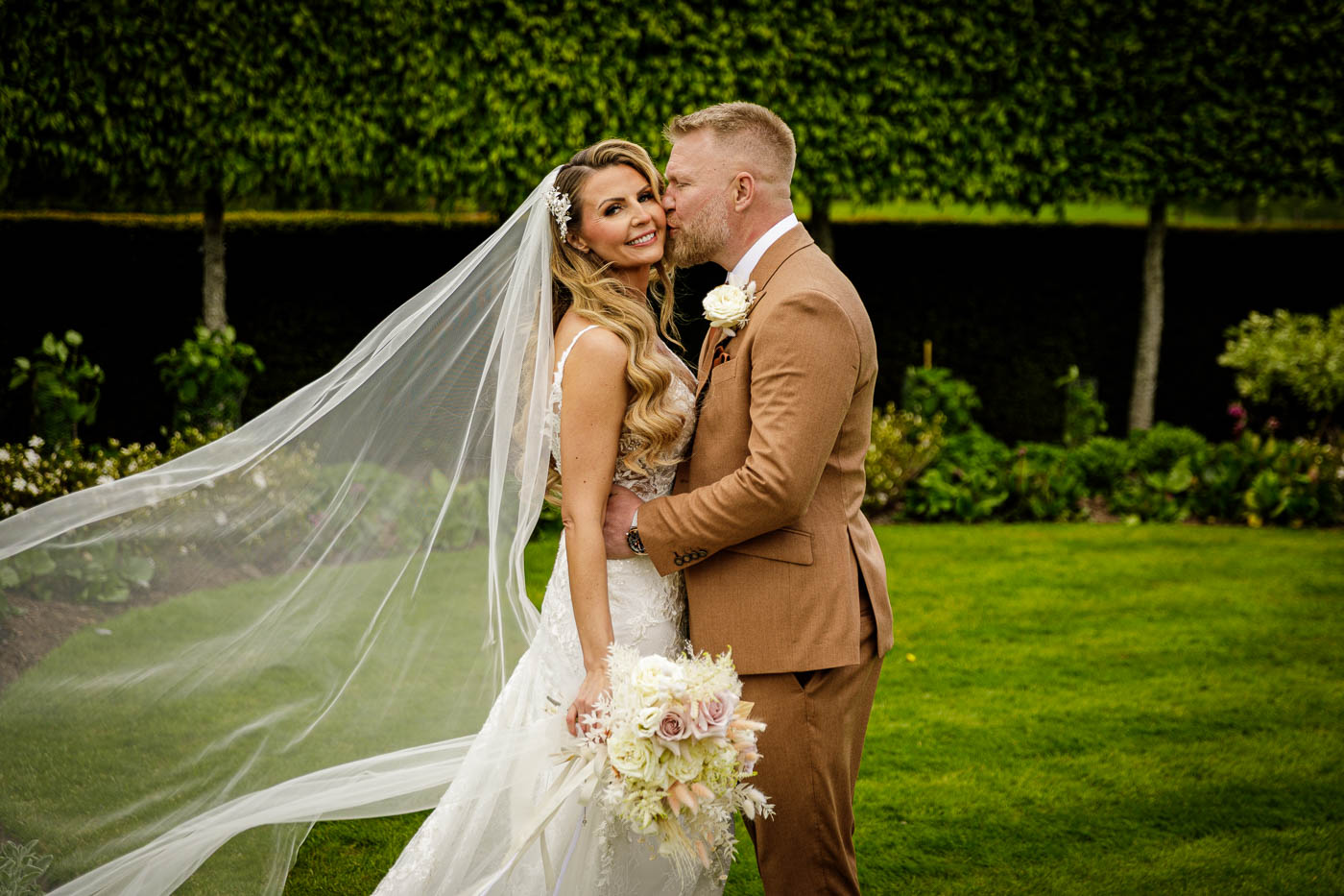 groom kissing smiling bride's cheek in gardens at merrydale