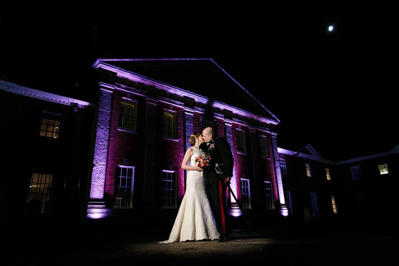 night photo bride and groom kissing in front of mottram hall